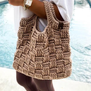 May include: A brown crocheted tote bag with a woven pattern. The bag has a single strap and a brown leather tag.