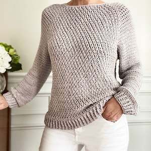 May include: A light gray crocheted sweater with a loose fit and long sleeves. The sweater has a simple, open stitch pattern.
