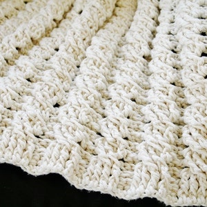 May include: A close-up of a crocheted blanket made with thick, white yarn. The blanket has a textured, woven pattern.