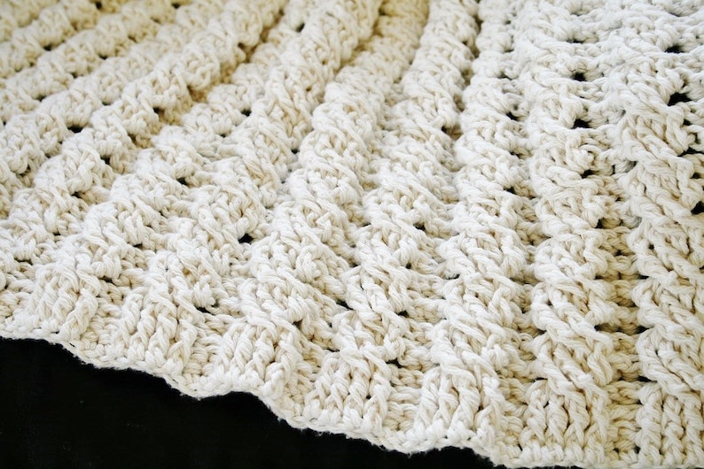 May include: A close-up of a crocheted blanket made with thick, white yarn. The blanket has a textured, woven pattern.