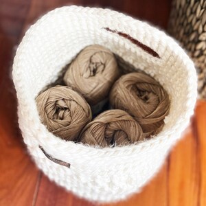 May include: A white crocheted basket with four balls of brown yarn inside.