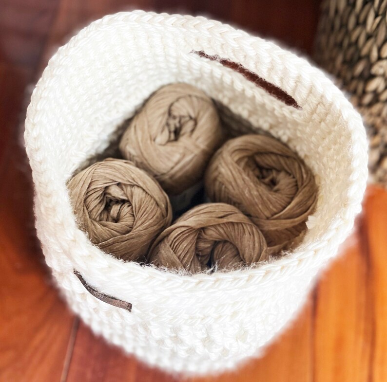 May include: A white crocheted basket with four balls of brown yarn inside.