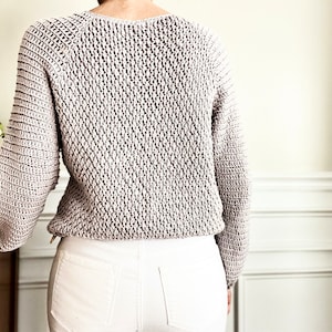 May include: A light gray knitted sweater with a textured stitch pattern. The sweater has a round neckline and long sleeves.