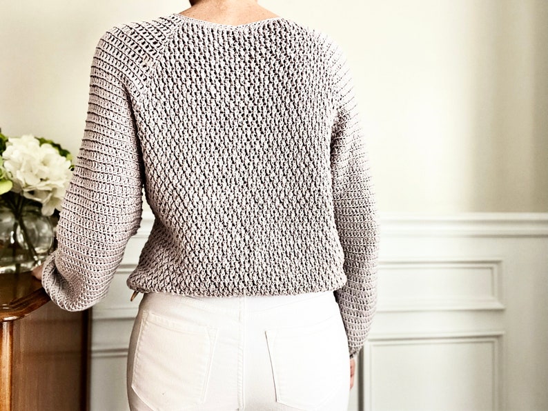 May include: A light gray knitted sweater with a textured stitch pattern. The sweater has a round neckline and long sleeves.