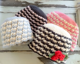 Può includere: Quattro cappelli all'uncinetto in diverse combinazioni di colori. I cappelli sono realizzati con un filato bianco e grigio, un filato rosa e bianco, un filato marrone e bianco e un filato nero e bianco. Uno dei cappelli ha un fiocco di fiori rosso.