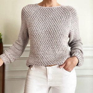 May include: A light gray knitted sweater with a loose fit and a round neckline. The sweater has a textured pattern and long sleeves.