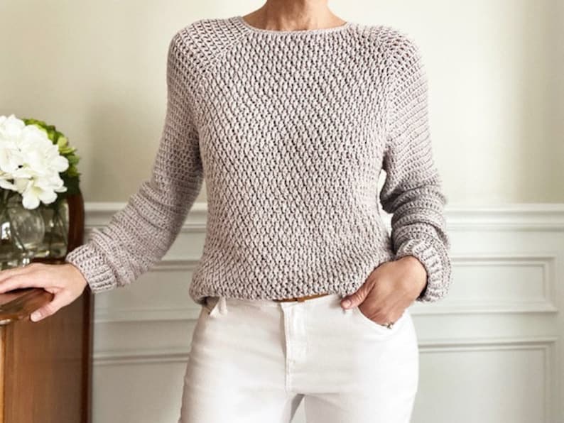 May include: A light gray knitted sweater with a loose fit and a round neckline. The sweater has a textured pattern and long sleeves.