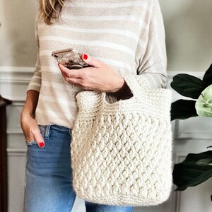 May include: A white crocheted tote bag with a textured pattern. The bag has a wide, flat base and a single handle.