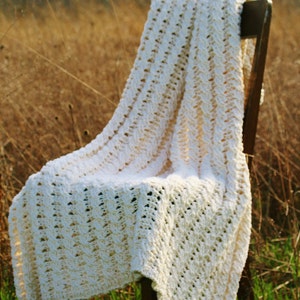 May include: A white crocheted blanket draped over a wooden chair in a field of tall grass.
