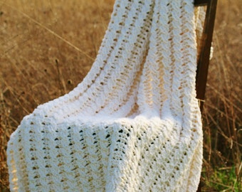 May include: A white crocheted blanket draped over a wooden chair in a field of tall grass.