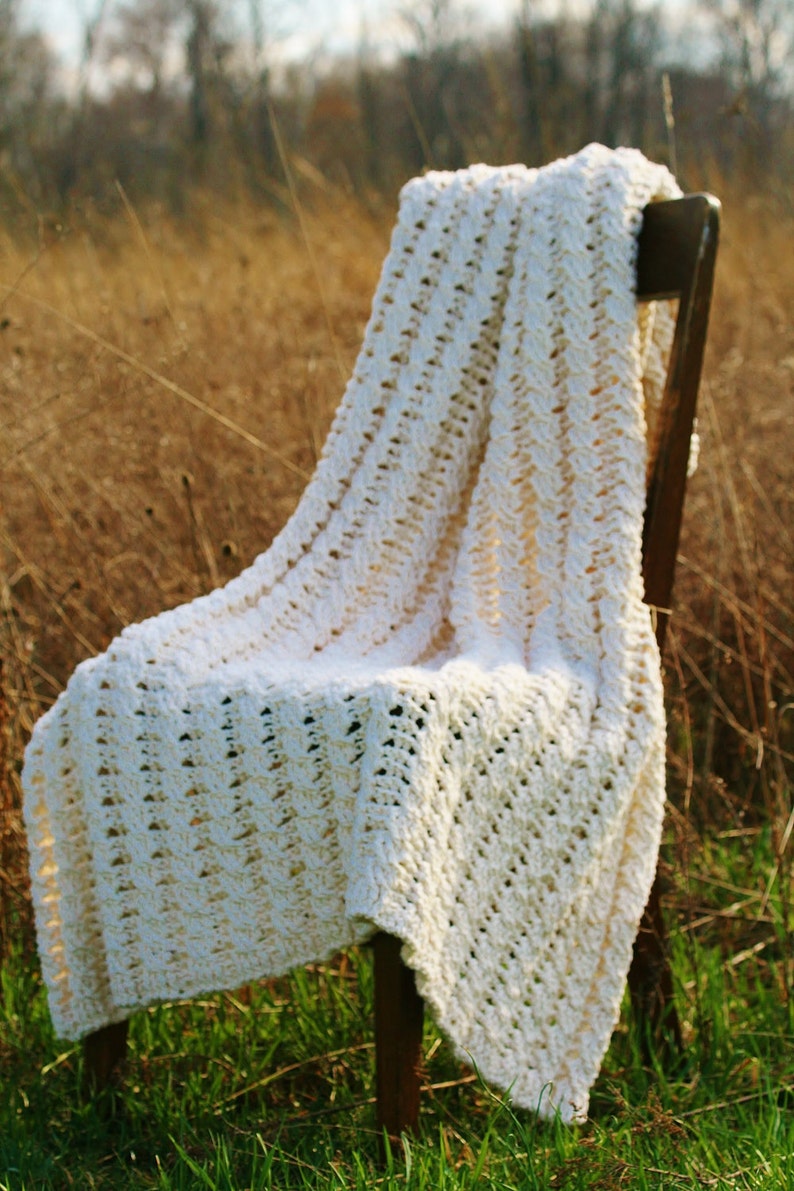 May include: A white crocheted blanket draped over a wooden chair in a field of tall grass.