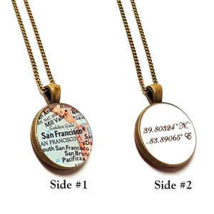 May include: A gold chain necklace with a round pendant. One side of the pendant features a map of San Francisco, California. The other side of the pendant has the coordinates 39.80324°N, -83.89065°E.