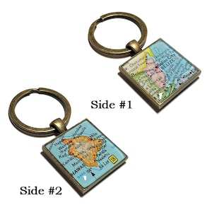 Könnte beinhalten: Zwei quadratische Schlüsselanhänger mit bronzefarbenen Ringen. Ein Schlüsselanhänger zeigt eine Karte von Belize, der andere eine Karte von Hawaii. Die Karten sind in einem quadratischen, bronzefarbenen Rahmen eingefasst. Der Text "Side #1" und "Side #2" ist sichtbar.