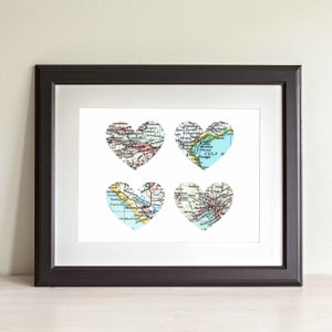 May include: A framed print featuring four heart-shaped maps. Each heart is a different colour and depicts a different city or region. The hearts are arranged in a grid pattern on a white background.