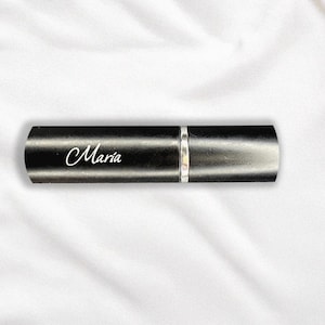 May include: A black perfume atomizer with a silver band and rounded ends. The name "Maria" is written in white script on the atomizer. The item is presented on a white, textured background.
