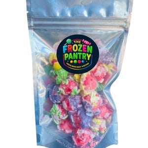 Può includere: Un sacchetto trasparente e richiudibile pieno di snack colorati liofilizzati. Gli snack sono un mix di rosso, viola, giallo e verde, con un logo che dice "The Frozen Pantry". Il sacchetto è sigillato e pronto per essere consumato.