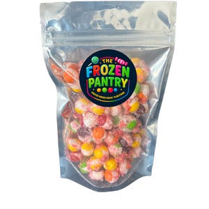 Può includere: Un sacchetto trasparente e richiudibile pieno di caramelle colorate liofilizzate. Il sacchetto presenta un'etichetta circolare con la scritta "THE FROZEN PANTRY" in blu, verde e giallo, con lo slogan "FREEZE DRIED SNAX 'N BEYOND". Le caramelle sono un mix di rosso, arancione, giallo e bianco.