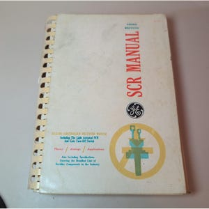 May include: A white spiral-bound technical book titled SCR MANUAL THIRD EDITION with red and blue text. The cover features a General Electric logo and a yellow circular graphic containing a blue and green schematic of a rectifier component.