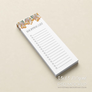 May include: A white notepad with the text "SHOPPING LIST" at the top. The top edge features a floral design in shades of yellow, pink, and green. The notepad measures approximately 8.9 x 21.6 cm and has lines and circles for check boxes.