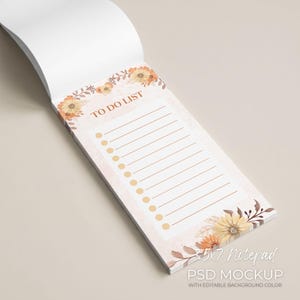 Puede incluir: Un bloc de notas de 3,5 x 7 pulgadas con un diseño floral. El bloc de notas presenta las palabras "TO DO LIST" en la parte superior, con líneas y círculos de verificación. El diseño floral incluye flores naranjas y amarillas con hojas marrones. El bloc de notas está sobre un fondo beige claro.