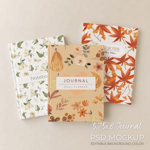 May include: Three journals with floral and autumn designs. The journals include a notebook with white flowers, a journal with a pumpkin and floral design, and a journal with orange leaves. The journals are 14.6 x 20.3 cm.