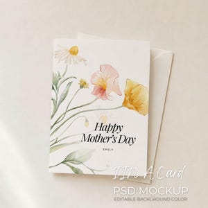 Puede incluir: Tarjeta de felicitación blanca con ilustraciones florales en acuarela y el texto "Happy Mother's Day". La tarjeta presenta flores amarillas y rosas, con un sobre a juego.