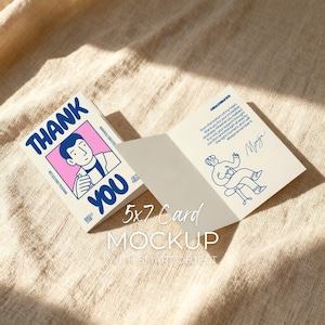 May include: A folded 5x7 card mockup with a "THANK YOU" design. The card features a cartoon illustration of a person and text. The open card displays a message and a drawing of a person on a chair. The background is a beige fabric.