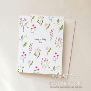 Puede incluir: Tarjeta de felicitación blanca con un diseño floral de flores y hojas rosas, rojas y verdes. La tarjeta dice "happy birthday dear". Se ve un sobre crema. La tarjeta mide 10,8 x 14 cm.