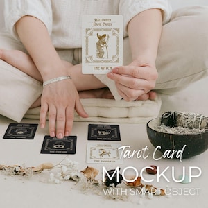 May include: A person holds a Halloween-themed tarot card labelled "The Witch," with other cards displaying titles like "The Zombie" and "The Potion." The cards are arranged on a white surface, with a decorative bowl and dried botanicals. The words "Tarot Card MOCKUP" are visible.