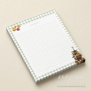 May include: A lined notepad with a green plaid border and a Christmas theme. The notepad features a small Christmas tree illustration with ornaments and a gold star. The text "merry christmas!" is written in gold script.