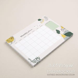 May include: A rectangular notepad with a monthly planner layout. The notepad is 11 x 8.5 inches and features a light gray background with abstract botanical designs in yellow, green, and black. Text on the notepad includes "Monthly planner" and "Monthly Goals".