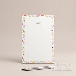 May include: A white notepad with a floral border in shades of pink, yellow, and purple. The word "notes" is written in green script. A silver pen rests below the notepad. The notepad measures 5.5 x 8.5 inches.