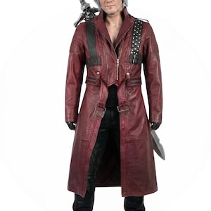 May include: A burgundy leather coat with a zipper closure, buckle accents, and black shoulder straps. The coat features a long length and a notched collar. A silver skull is attached to the shoulder. The person is wearing black gloves and holding a silver blade.