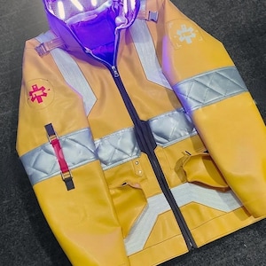 Puede incluir: Chaqueta amarilla con detalles plateados y blancos, cremallera negra y capucha con luz morada. La chaqueta tiene un símbolo médico rojo y blanco en el pecho y el brazo. Tiene dos bolsillos y una correa roja.