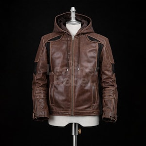 May include: Brown leather jacket with a hood and a zipper closure. The jacket has black accents on the shoulders and sleeves. The jacket is displayed on a mannequin against a black background.