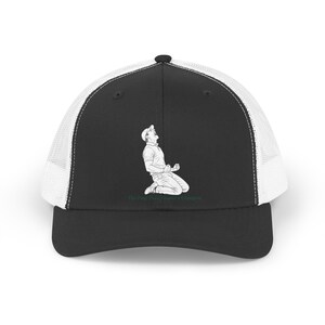 May include: Black and white trucker hat with a line drawing of a golfer celebrating. The hat has a black front panel and peak, with a white mesh back. The text "The Final Putt, Starts a Champion" is printed on the brim.