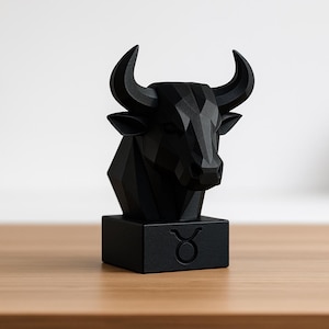 Op de afbeelding: Zwarte geometrische sculptuur van een stierenkop met hoorns, gemonteerd op een vierkante basis. De basis toont het sterrenbeeld Stier. De sculptuur wordt gepresenteerd op een houten oppervlak.