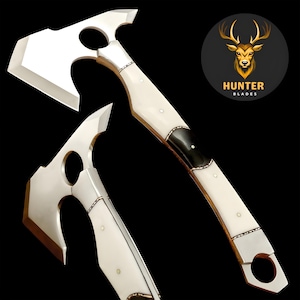 Könnte beinhalten: Ein poliertes Tomahawk aus Stahl mit weißem Griff und schwarzen Akzenten. Das Tomahawk hat ein kreisförmiges Loch in der Nähe des Griffs und eine gebogene Klinge. Das Bild enthält das Hunter Blades Logo.