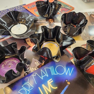Peut inclure: Cinq bols en vinyle noir avec des motifs différents. Les bols sont fabriqués à partir de disques vinyles recyclés et ont un aspect unique et fait main. Les bols sont posés sur des pochettes d'albums.