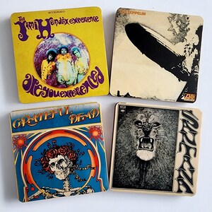 May include: Four vintage vinyl record album covers. The top left cover is yellow with the text "The Jimi Hendrix Experience Are You Experienced". The top right cover is beige with the text "Led Zeppelin". The bottom left cover is blue with the text "Grateful Dead". The bottom right cover is white with the text "Santana".
