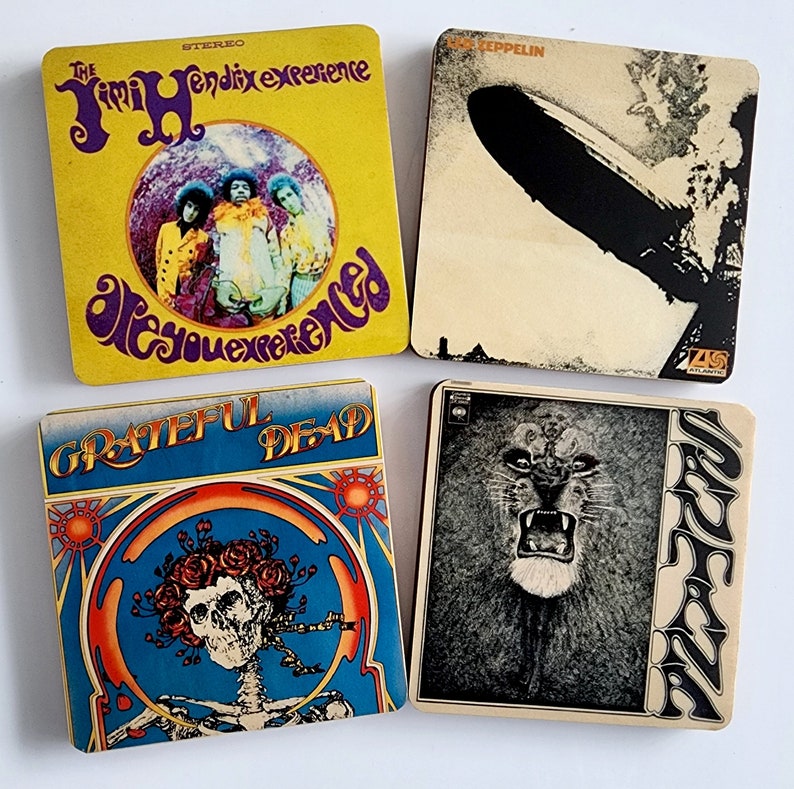May include: Four vintage vinyl record album covers. The top left cover is yellow with the text "The Jimi Hendrix Experience Are You Experienced". The top right cover is beige with the text "Led Zeppelin". The bottom left cover is blue with the text "Grateful Dead". The bottom right cover is white with the text "Santana".
