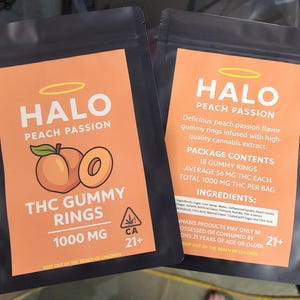 May include: Two black resealable pouches with orange labels. The front label reads HALO PEACH PASSION THC GUMMY RINGS 1000 MG with a peach graphic. The back label lists 18 gummy rings, 56 mg THC each, 1000 mg total, ingredients, and a 21+ warning.