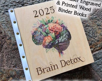 May include: A wooden binder book with a floral brain design and the text "2025" and "Brain Detox." The book has a white leather spine with gold rivets. The text "Custom Laser Engraved & Printed Wood Binder Books" is also visible.