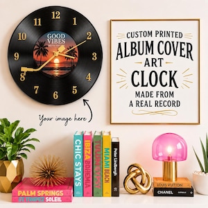 May include: A black vinyl record wall clock with gold numbers and hands, featuring a center image of a sunset over palm trees. Next to it, a framed sign reads: CUSTOM PRINTED ALBUM COVER ART CLOCK MADE FROM A REAL RECORD. Below, books and decor.