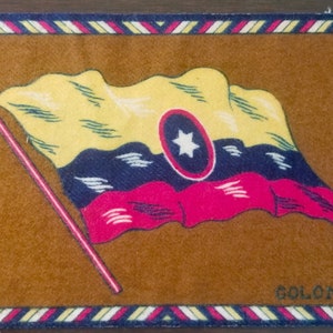 May include: A brown felt patch with a colorful embroidered flag of Colombia. The flag is yellow, blue, and red with a white star in a blue circle. The text "COLOMBIA" is embroidered in white at the bottom of the patch.