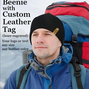 May include: A black beanie with a custom leather tag. The tag is laser engraved. The image also includes text that says "Beenie with Custom Leather Tag (laser engraved) Your logo or text any size any leather color."