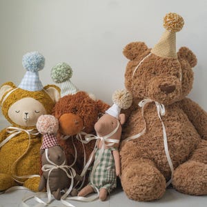 Puede incluir: Una colección de osos de peluche y figuras de animales, cada uno adornado con sombreros de fiesta y cintas. Los osos son de varios tonos de marrón y dorado, con texturas suaves y detalles caprichosos, perfectos para la habitación de un niño.