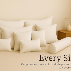 Puede incluir: Una colección de almohadas de color marfil en varias formas y tamaños, incluyendo rectangulares, cuadradas y cilíndricas. Las almohadas están dispuestas sobre una cama, con una pequeña mesita de noche de madera y un jarrón con flores secas en el fondo. El texto en la imagen dice "Every Size".