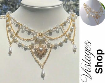 Puede incluir: Un collar de varias capas con perlas de imitación, cuentas transparentes y cadenas doradas. El collar presenta un colgante en forma de corazón con un centro de perla y gotas de perlas colgantes. El collar se exhibe en un maniquí blanco.