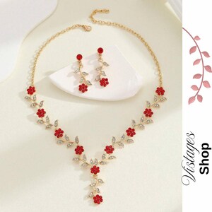 Può includere: Un set di collana e orecchini color oro. La collana e gli orecchini presentano accenti rossi a forma di fiore e abbellimenti trasparenti simili a cristalli. Il design floreale è incastonato su un metallo color oro. Gli orecchini pendono da una piccola catena d'oro.